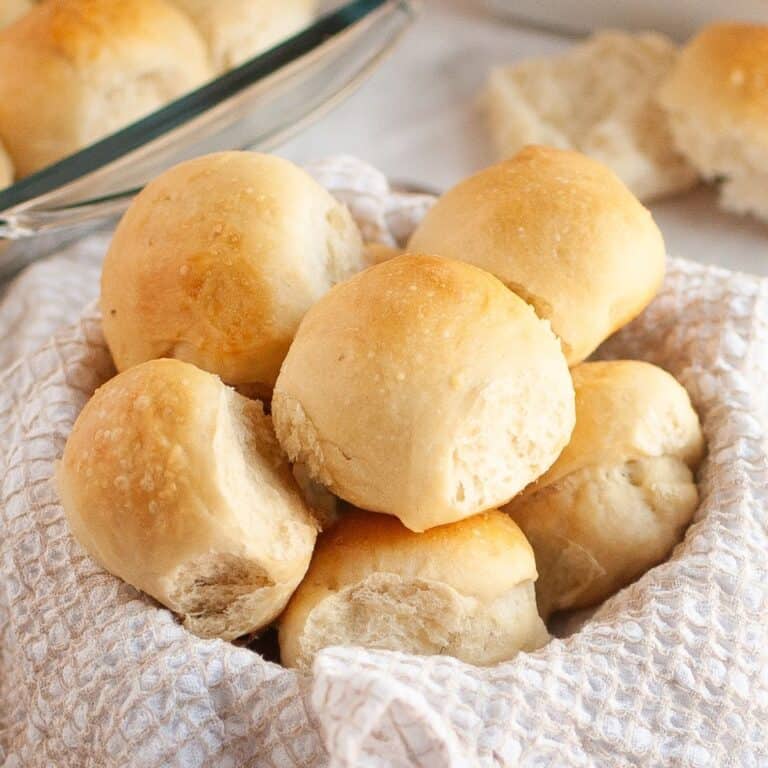 A basket lined with cloth filled with stacked sourdough brioche rolls.