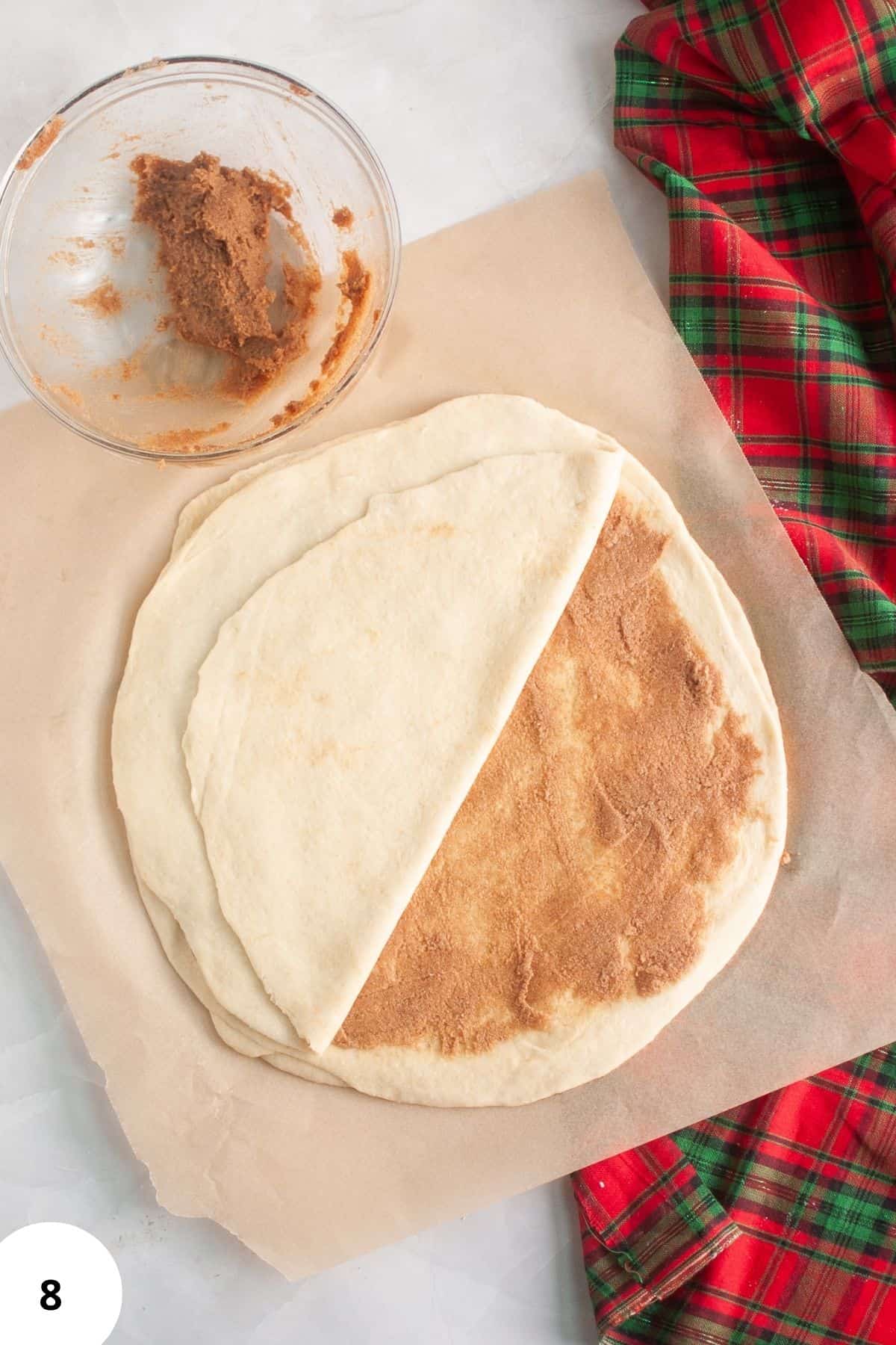 Bread dough being spread halfway with a buttery mixture during the preparation process.