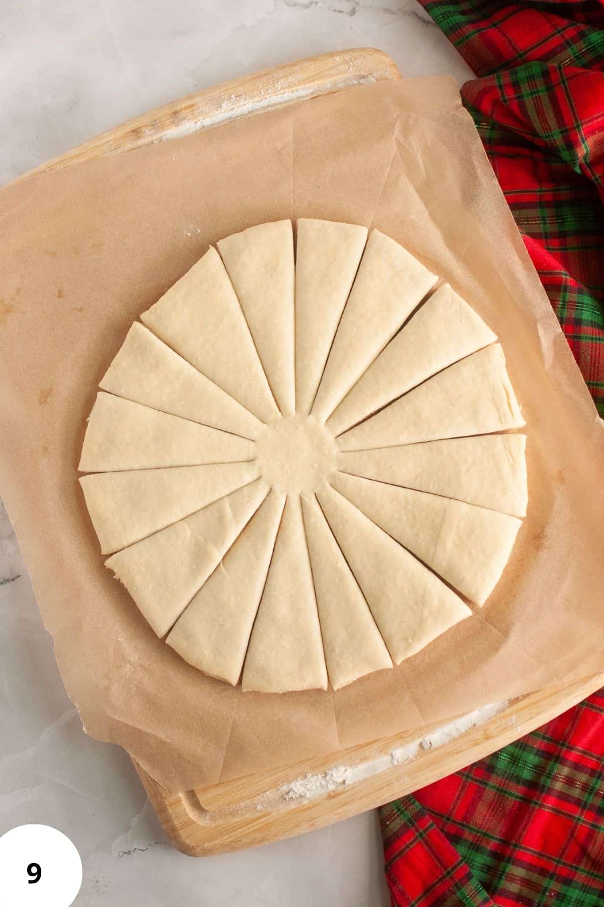 Bread dough placed on a wooden board being cut into triangular pieces for shaping.