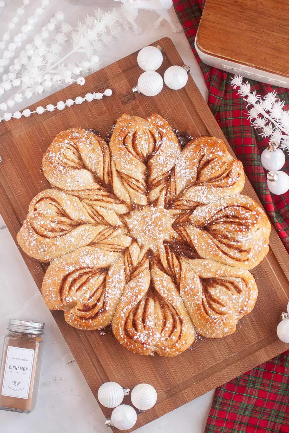 Homemade sourdough star bread displayed on a wooden board, surrounded by festive Christmas ornaments and holiday decorations.
