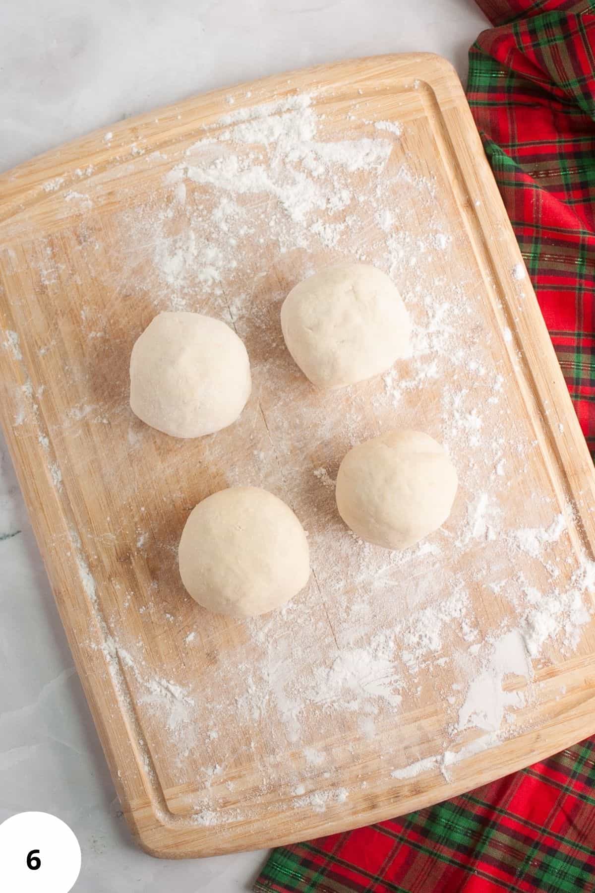 Dough shaped into a ball and lightly floured on a wooden surface during bread preparation.