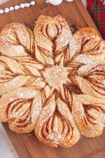 Homemade sourdough star bread displayed on a wooden board, surrounded by festive Christmas ornaments and holiday decorations.