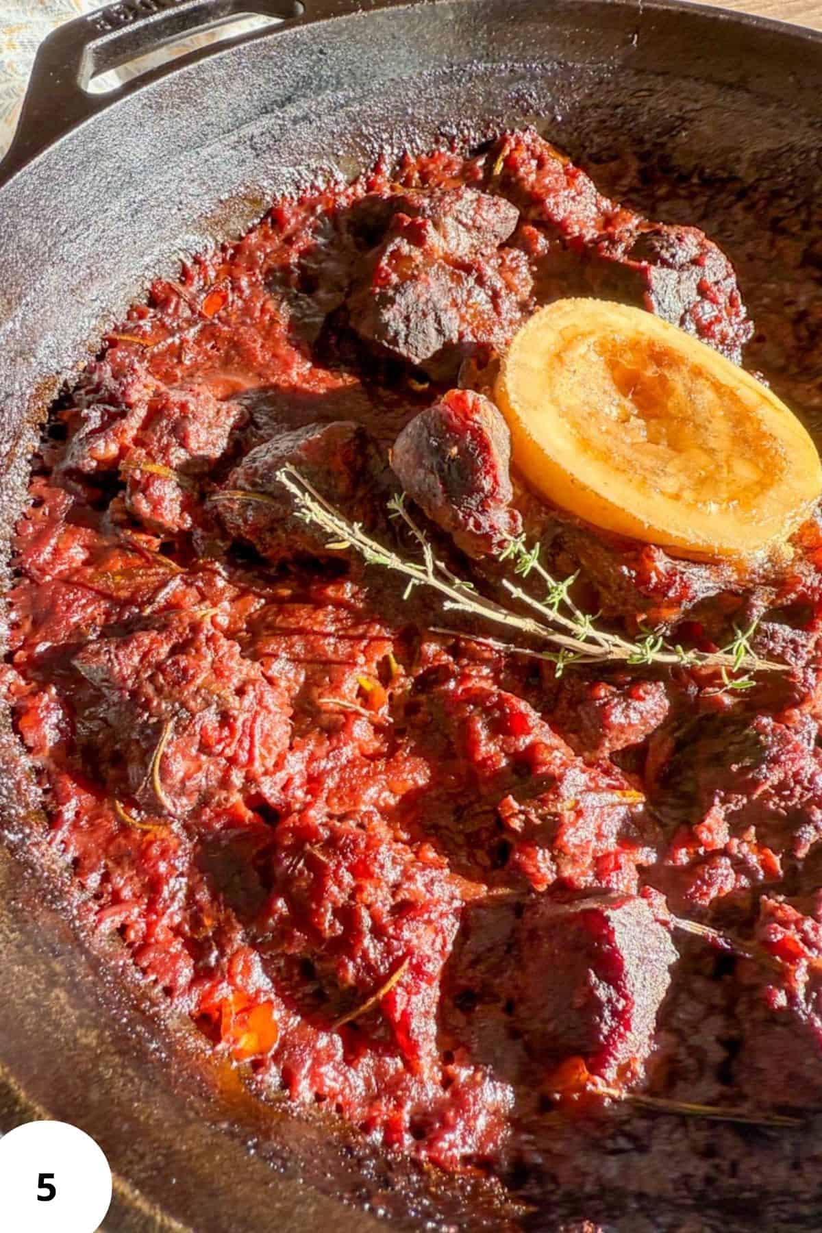 Close-up of Tuscan oven-braised beef in red wine, cooked in a cast iron skillet with herbs and sauce.