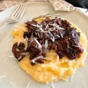 Delicious meat stew atop mashed potatoes garnished with cheese on a plate.