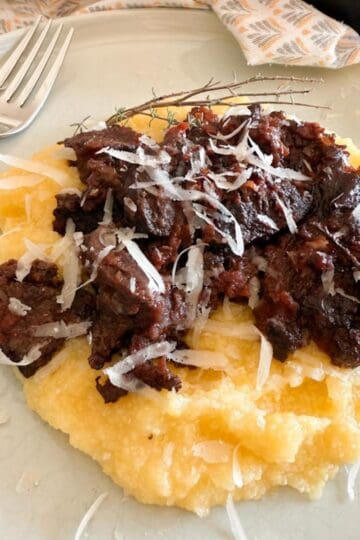 Tuscan oven-braised beef in red wine served on a plate over creamy mashed potato, with a fork on the side.