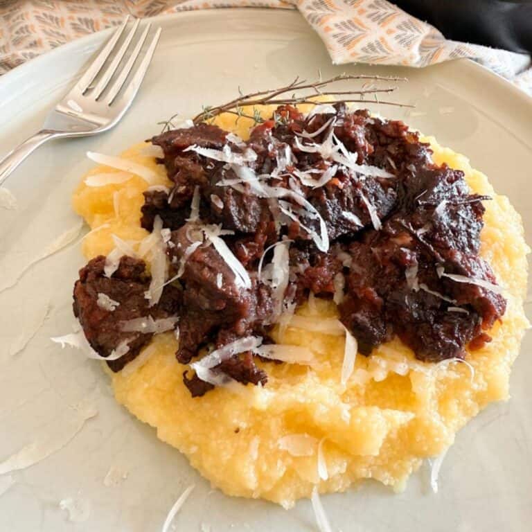 Delicious meat stew atop mashed potatoes garnished with cheese on a plate.