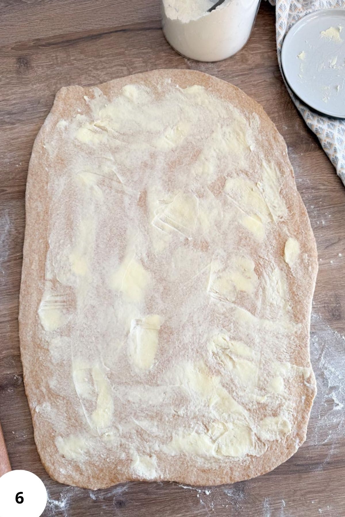 Sourdough cinnamon roll dough being spread with cinnamon-sugar mixture.