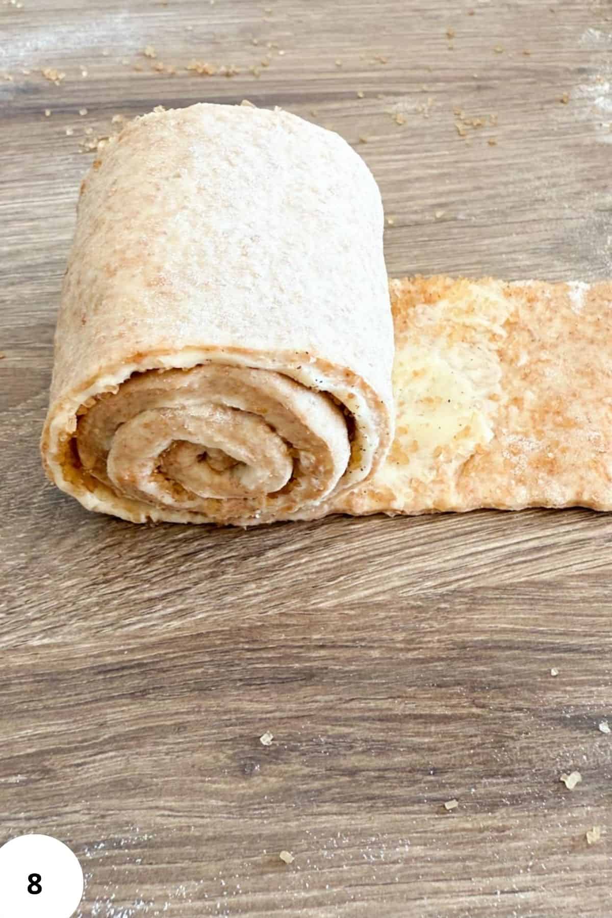 Sourdough cinnamon roll dough being rolled out on a floured surface.