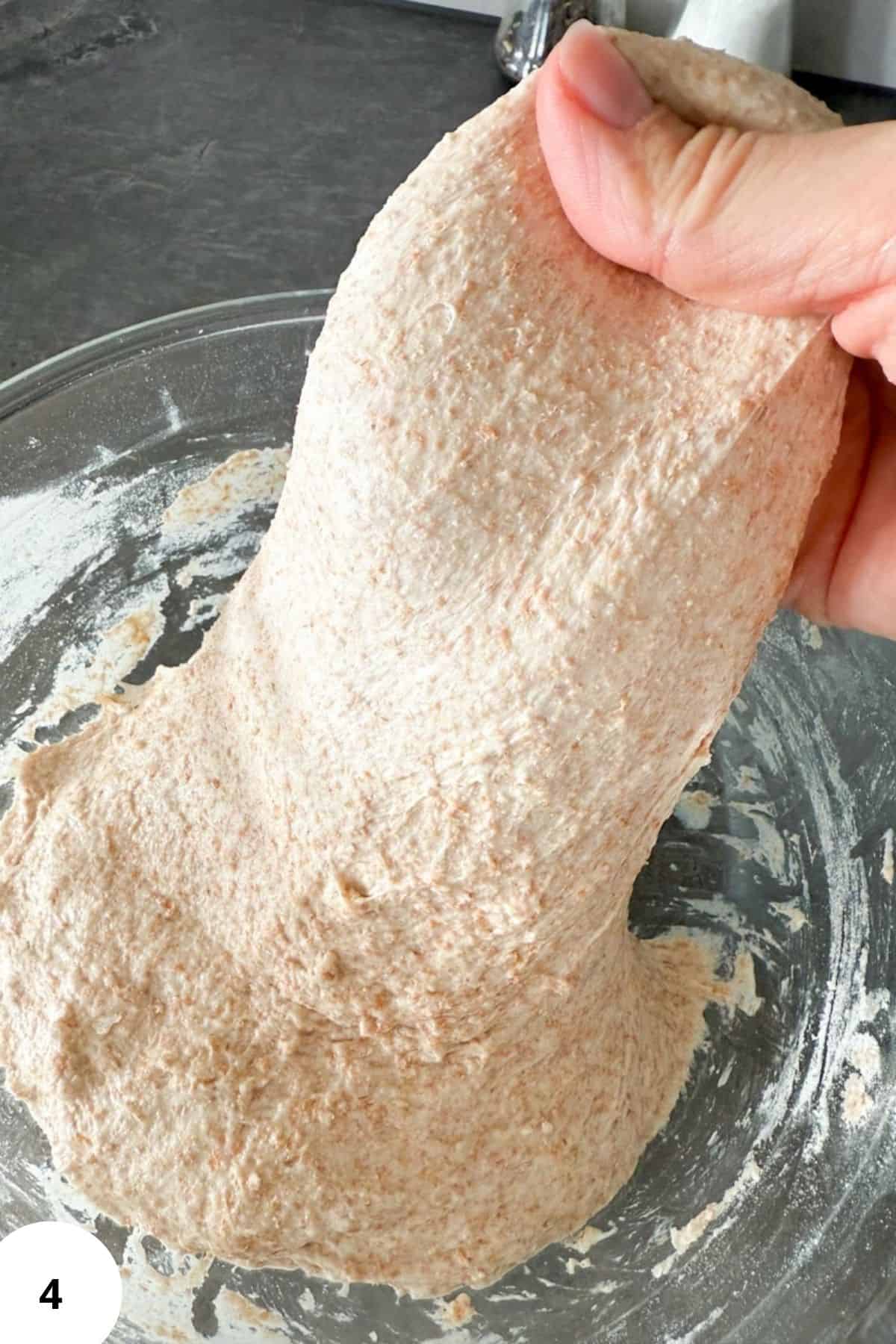 A hand stretching dough inside a large bowl during the sourdough folding process.