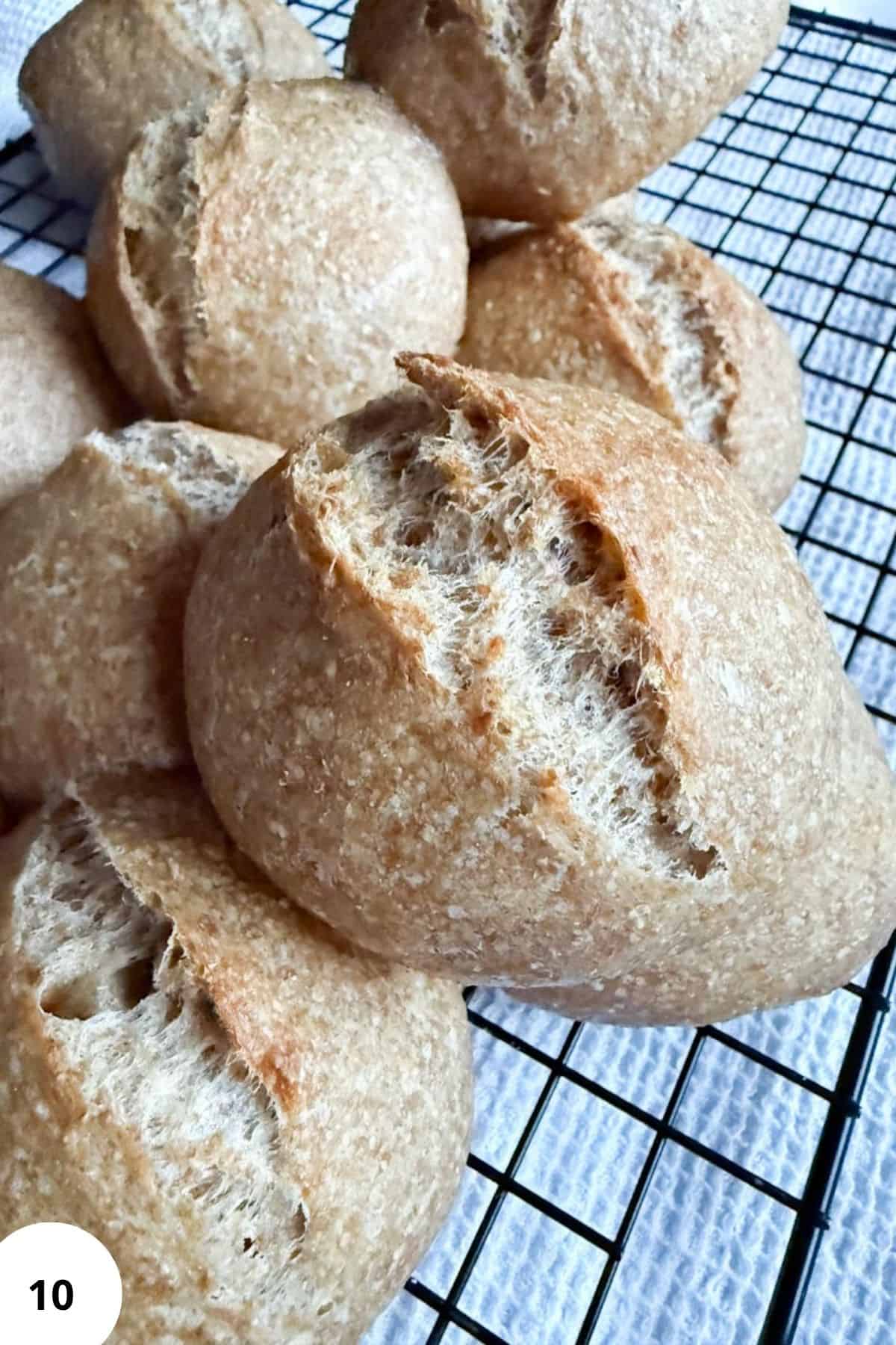 Freshly baked sourdough rolls resting on a wire cooling rack, showing their golden crust and airy texture.
