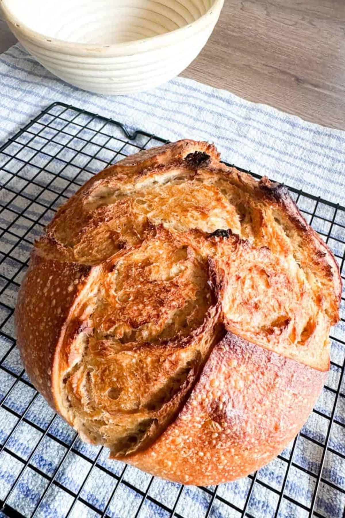 A freshly baked rustic sourdough bread loaf cooling on a wire rack, showcasing the artisanal bread baking process and crust texture.