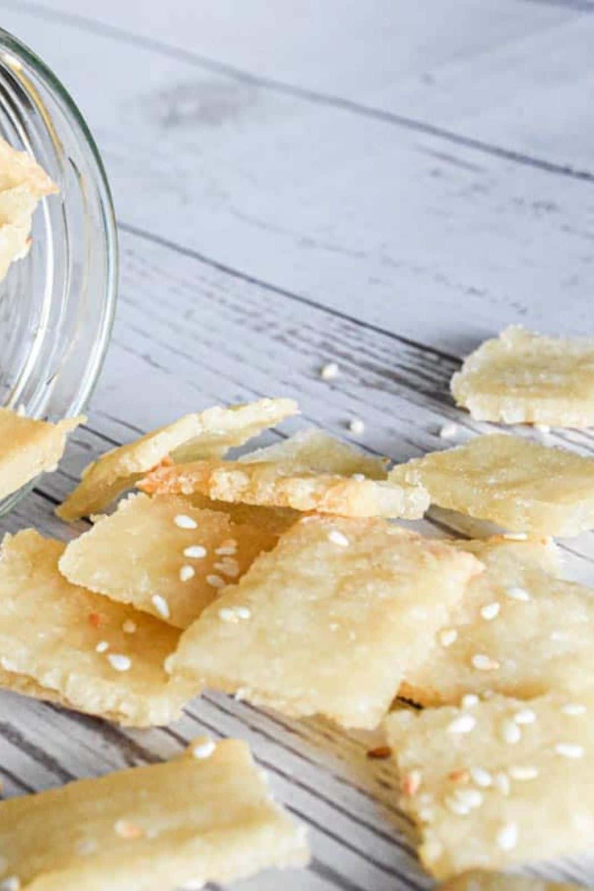 A jar of sourdough crackers with some crackers spread out on a surface beside it.