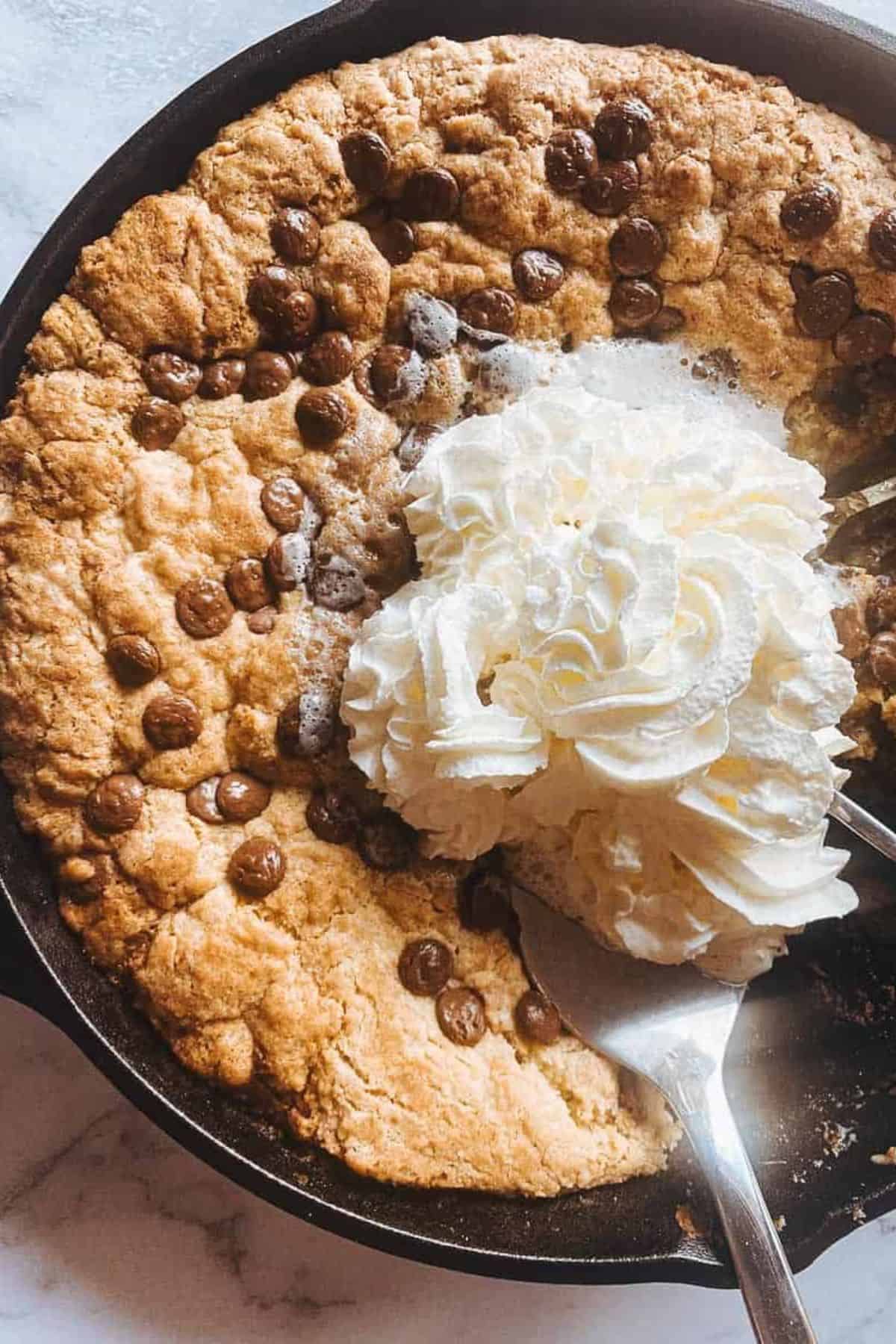 Sourdough chocolate chip cookie baked in a skillet, topped with whipped cream.