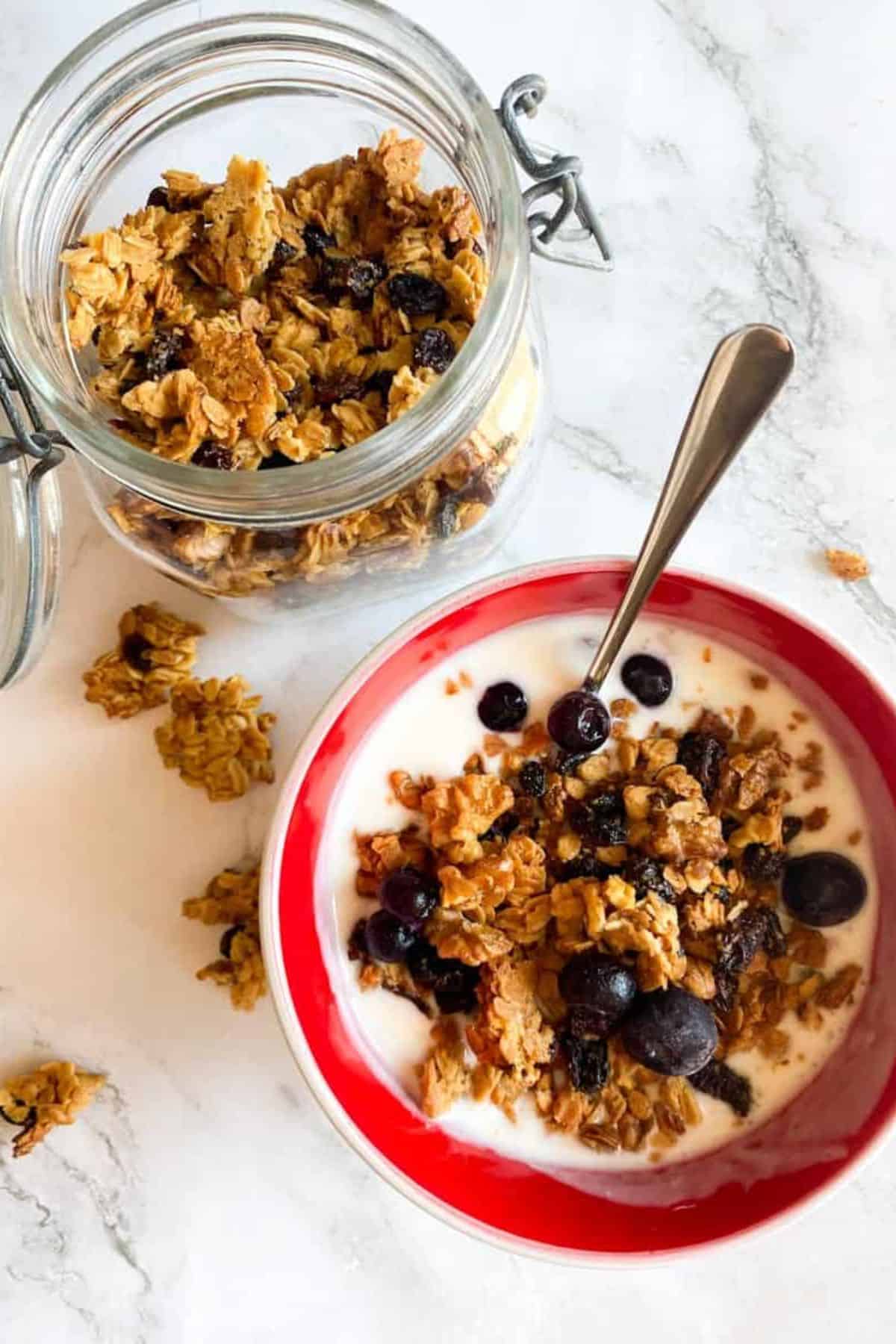 Sourdough granola served in a bowl with milk and a spoon, with extra granola stored in a glass jar nearby.