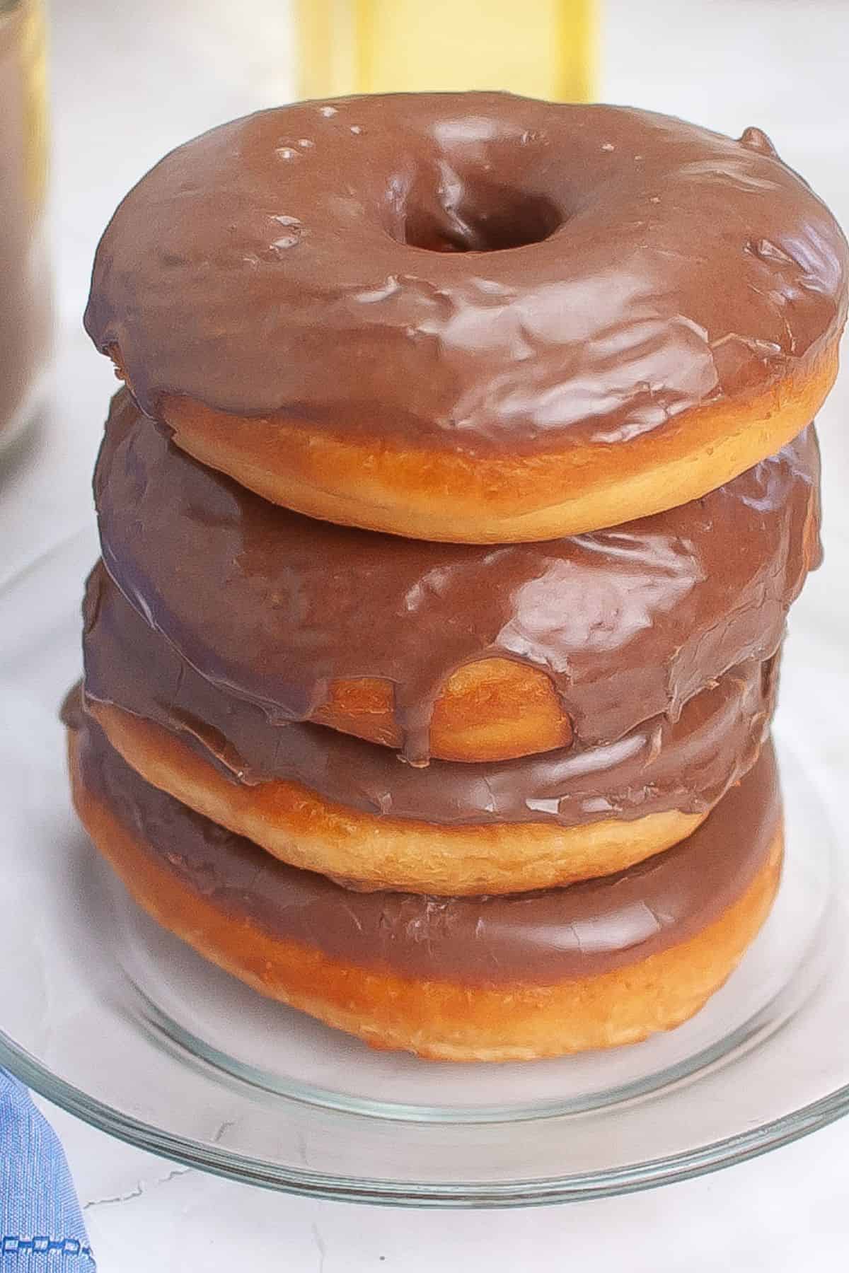 Chocolate glazed sourdough donuts stacked on a plate.