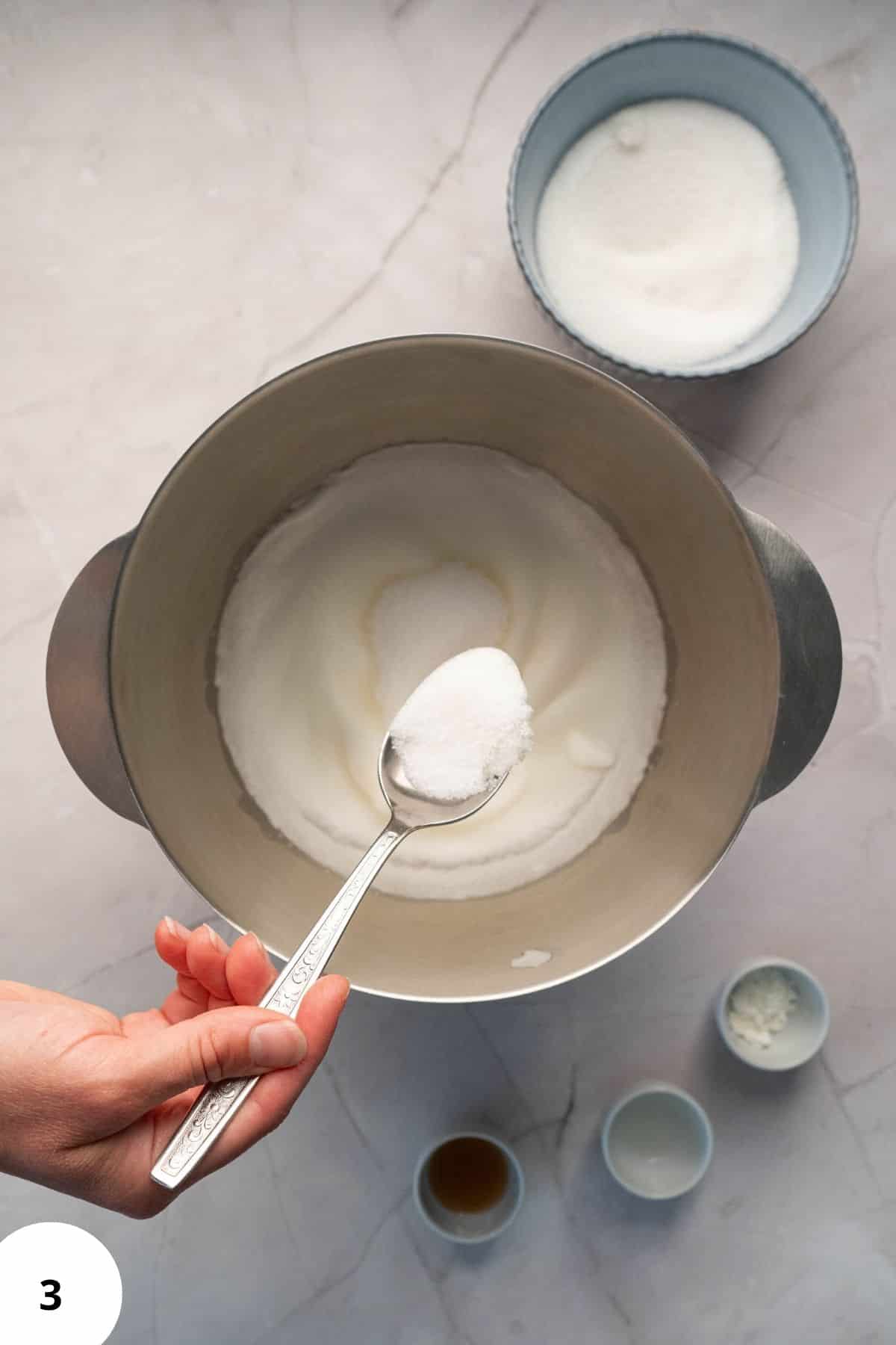 Spoon of sugar over mixture in mixing bowl.
