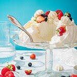 Sweet and creamy cheesecake decorated with strawberries, blueberries, and whipped cream on a glass cake stand.