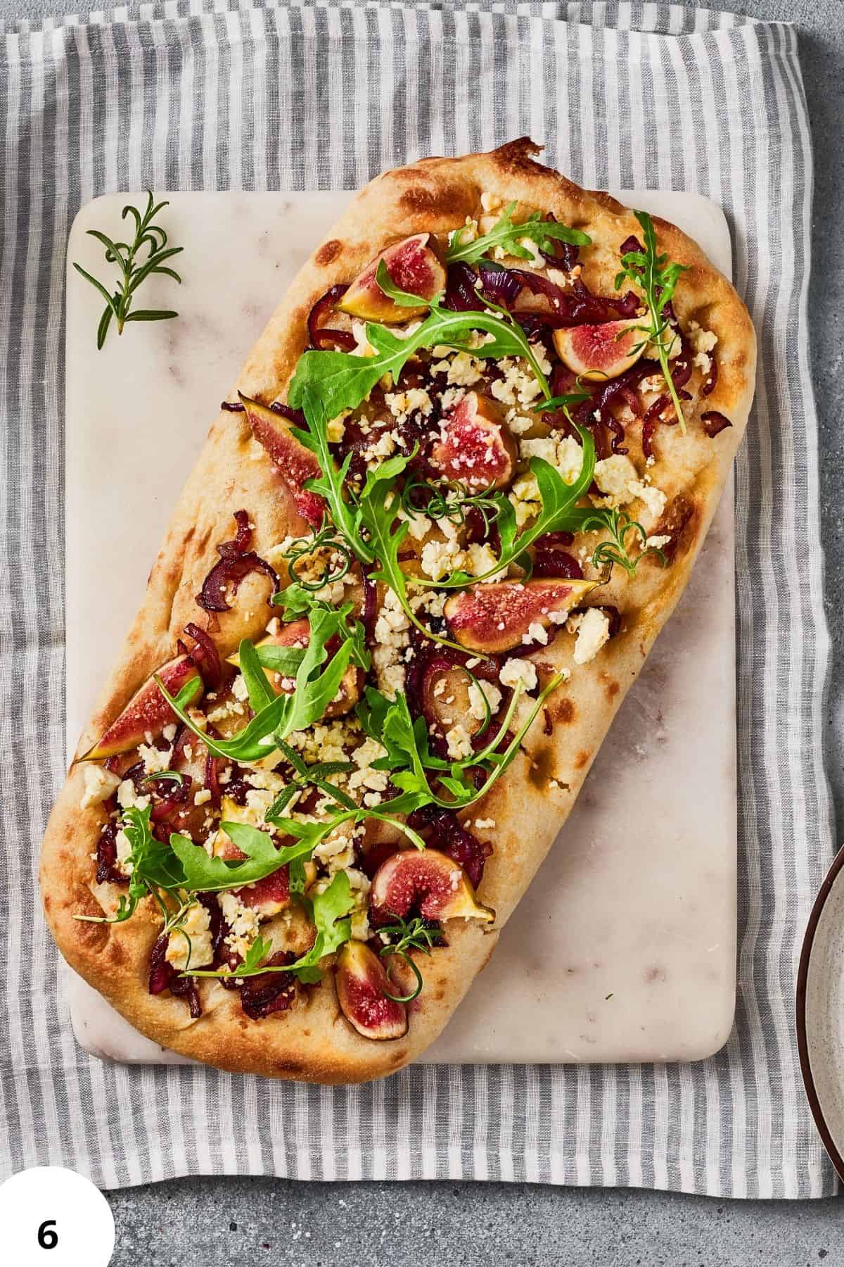 Delicious homemade bread topped with fresh figs, arugula, and cheese, showcasing kneading and shaping techniques.