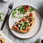Elegant focaccia with figs, arugula, and feta cheese, served on a stylish plate. Ideal for gourmet bread and artisanal pizza enthusiasts.