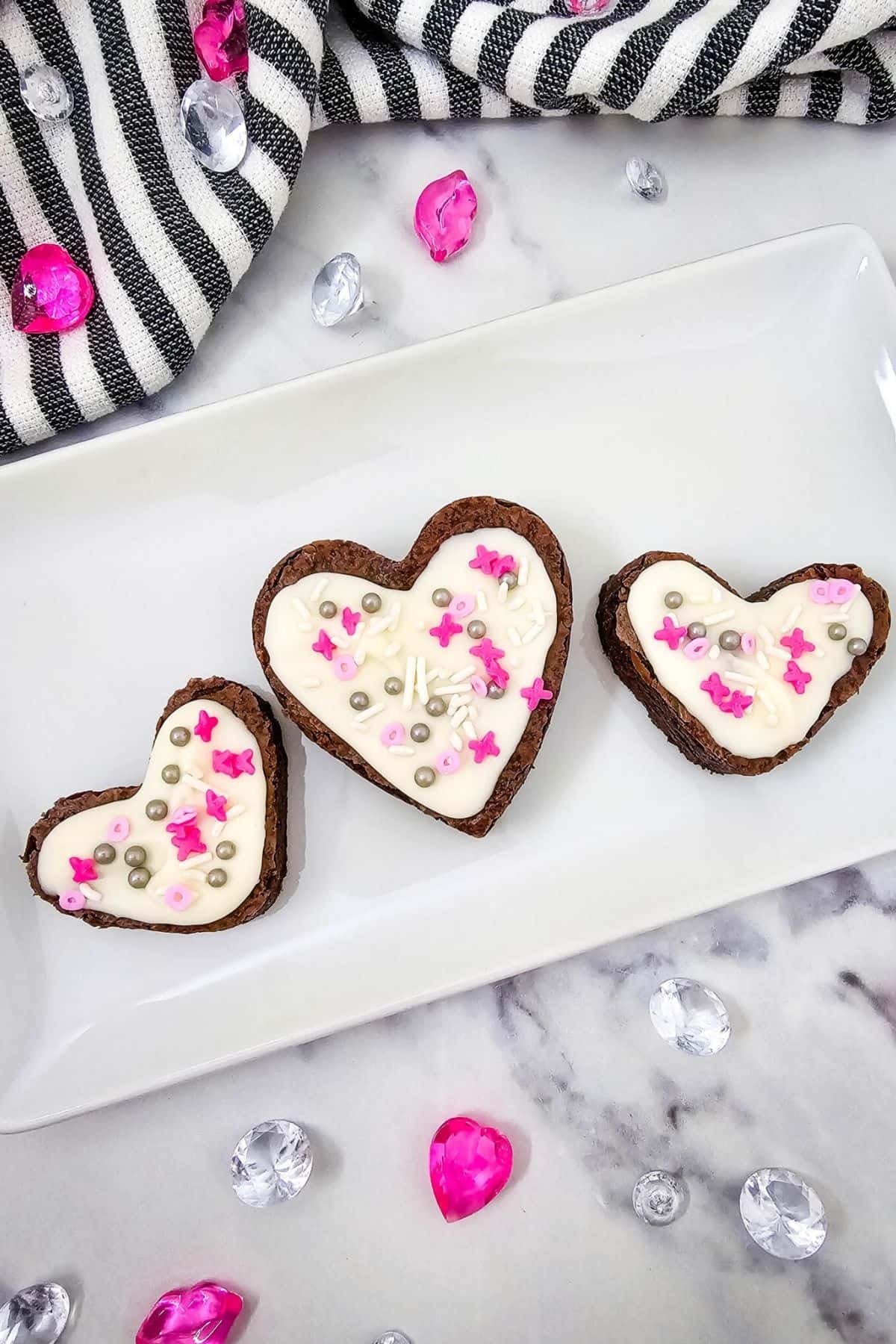 Delicious heart-shaped cookies with white frosting and pink sprinkles on a white plate.