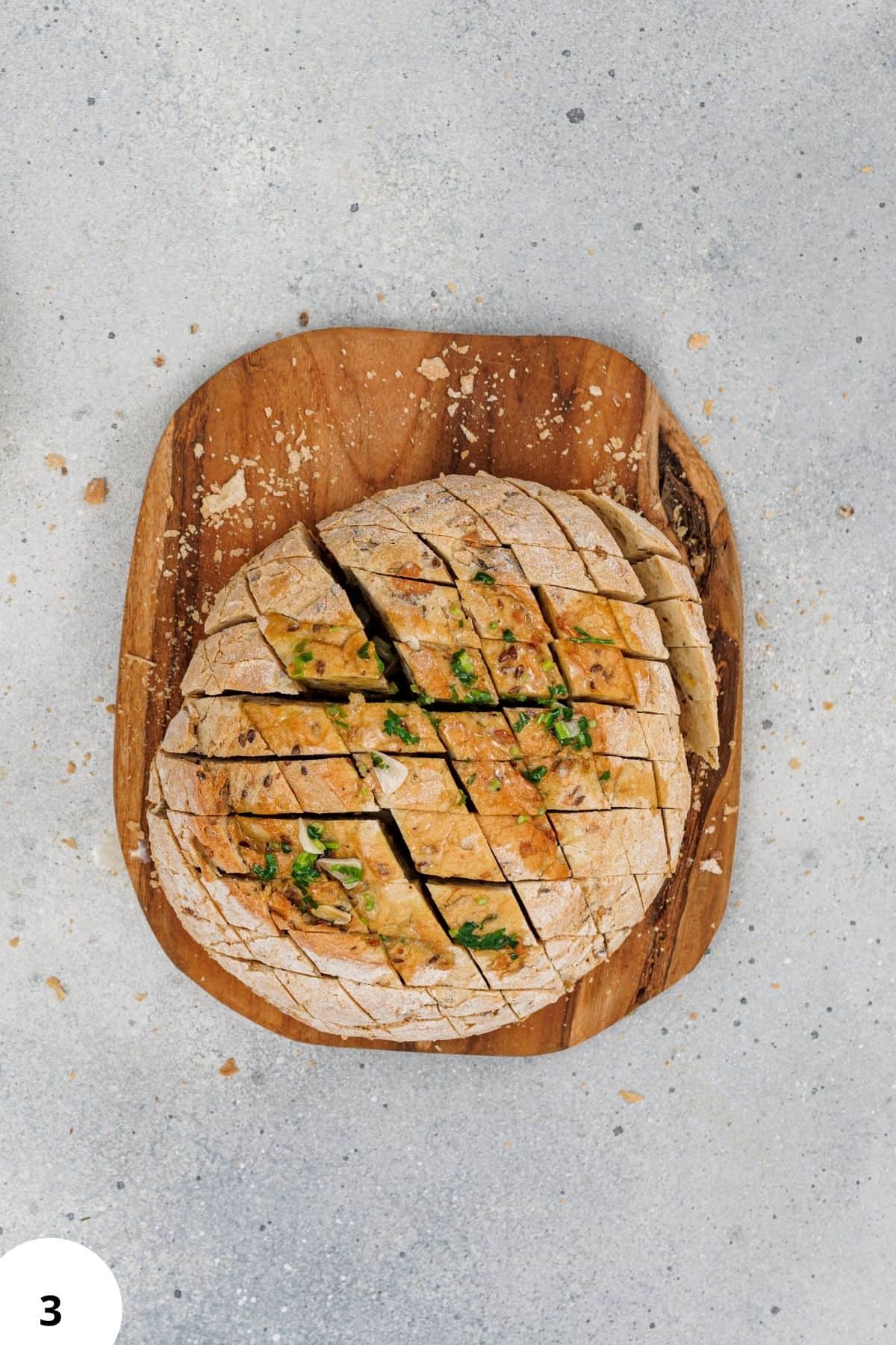 Artisan bread dough ready for baking, seasoned with herbs and scallions, on a rustic wooden cutting board.