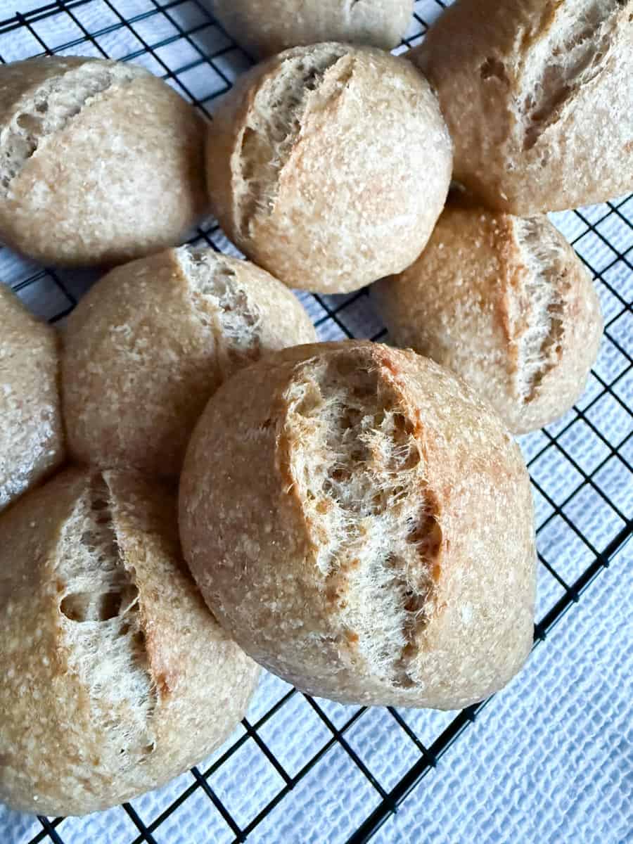 Golden-brown bread rolls cooling on a wire rack, showcasing crust and fluffy texture.