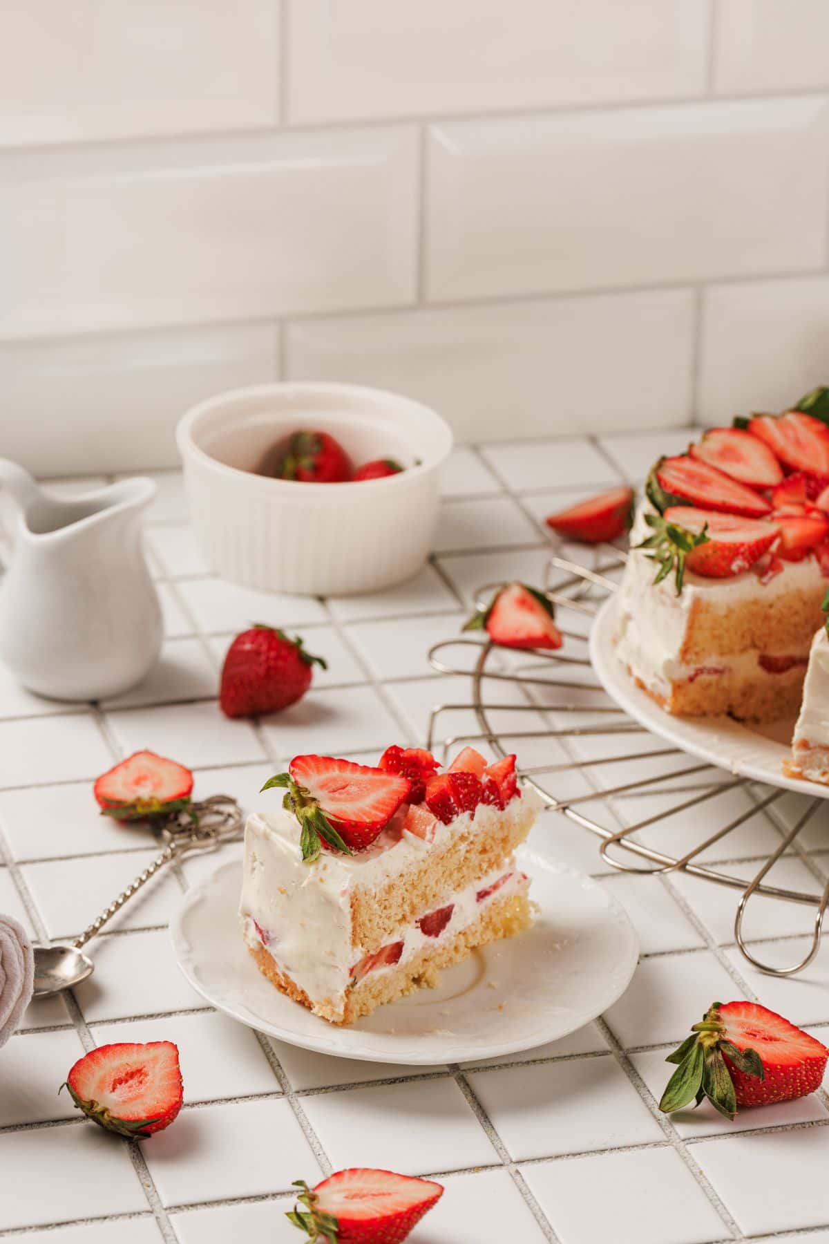 Delicious strawberry layer cake with cream cheese frosting, garnished with fresh strawberries on a white plate.