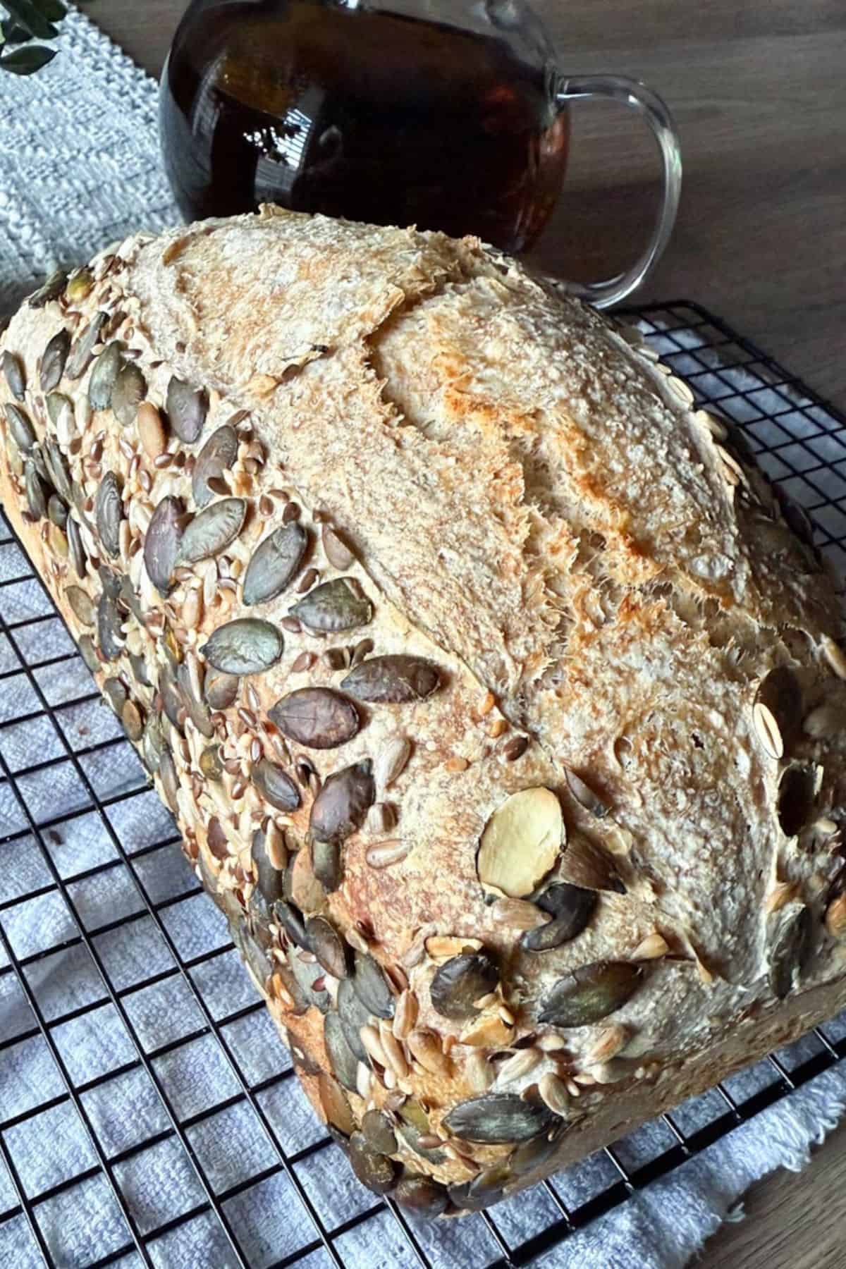 Artisan sourdough bread with pumpkin seeds on crust, cooling on a wire rack.
