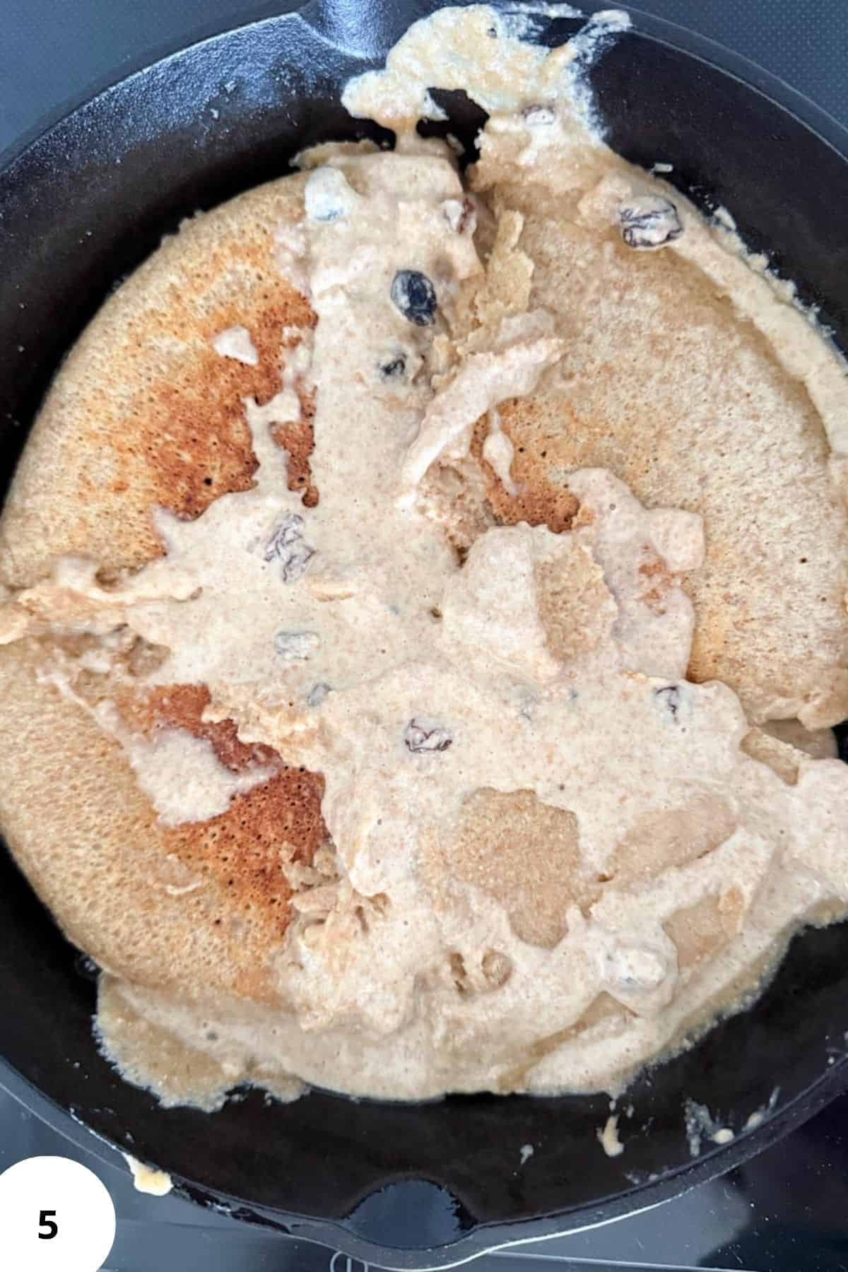 Cooking shredded pancake in a skillet with batter and blueberries.
