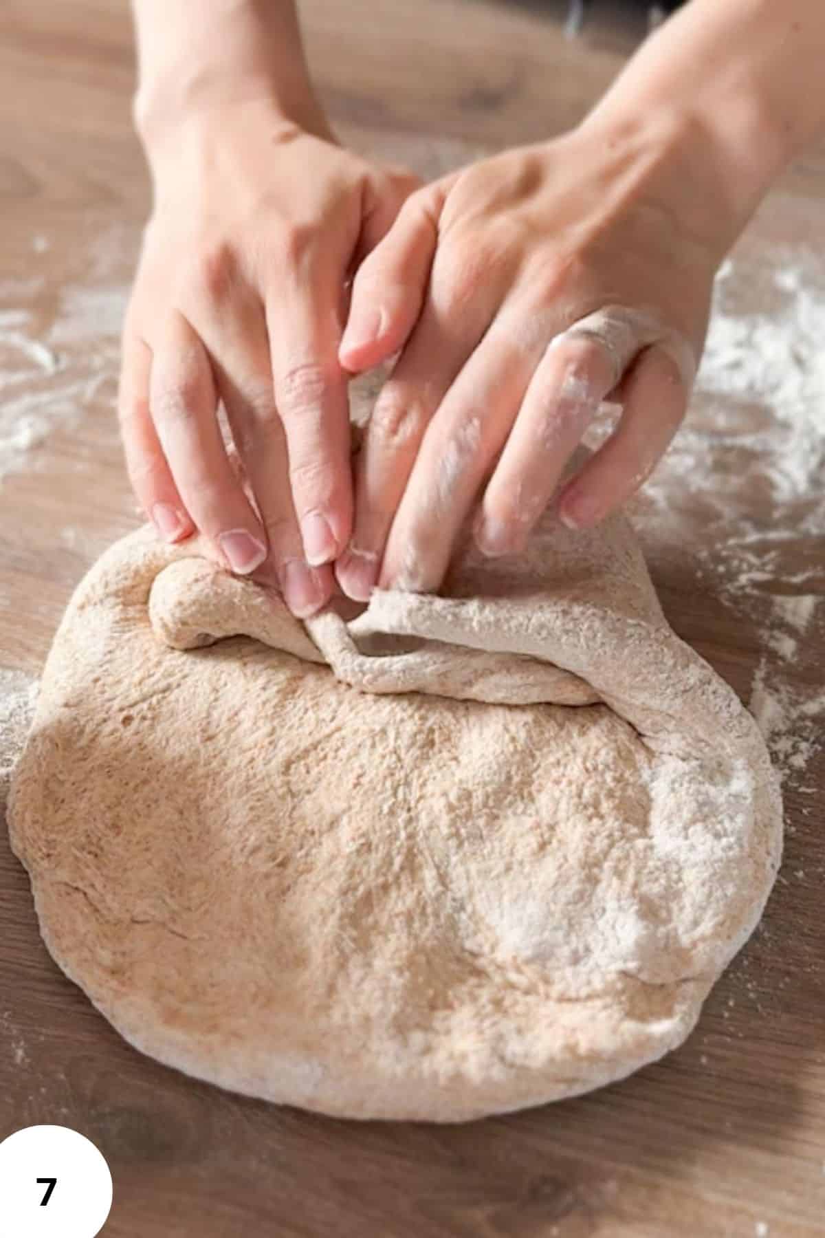 Hands performing stretch and fold technique on sourdough dough.