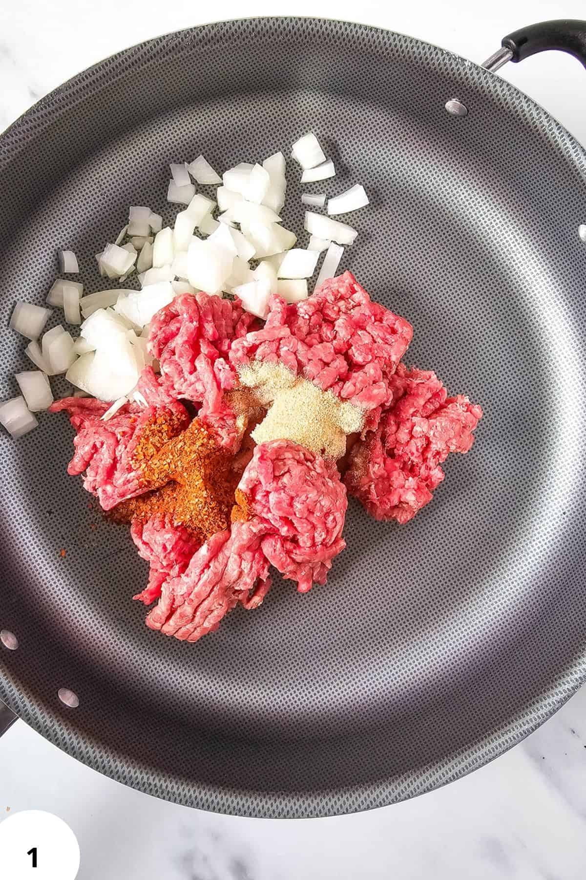 Close-up of ground beef, chopped onions, spices in a non-stick skillet.