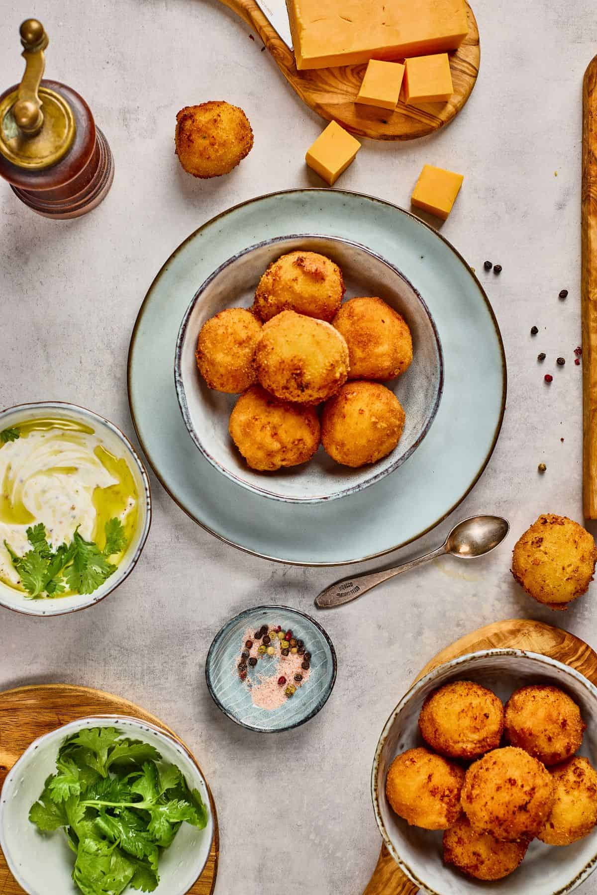 Alt text: Golden fried cheese balls served with cheese, herbs, and dipping sauces on a table.