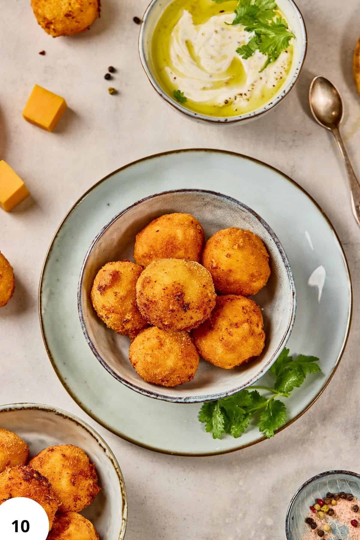Crispy cheese balls served with dipping sauce and garnished with fresh herbs.