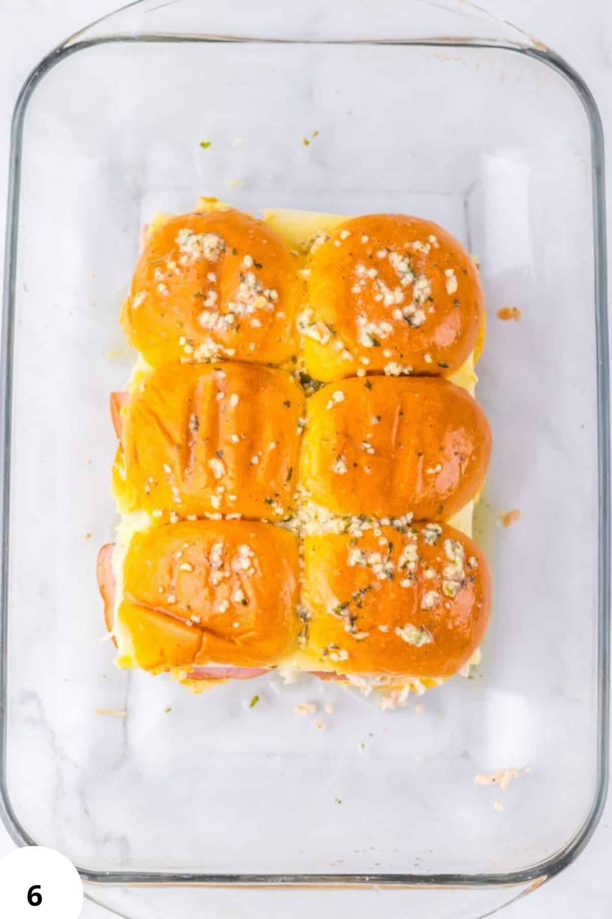 Homemade bread rolls with cheese, herbs, and butter in a glass baking dish, perfect for baked bread recipes.