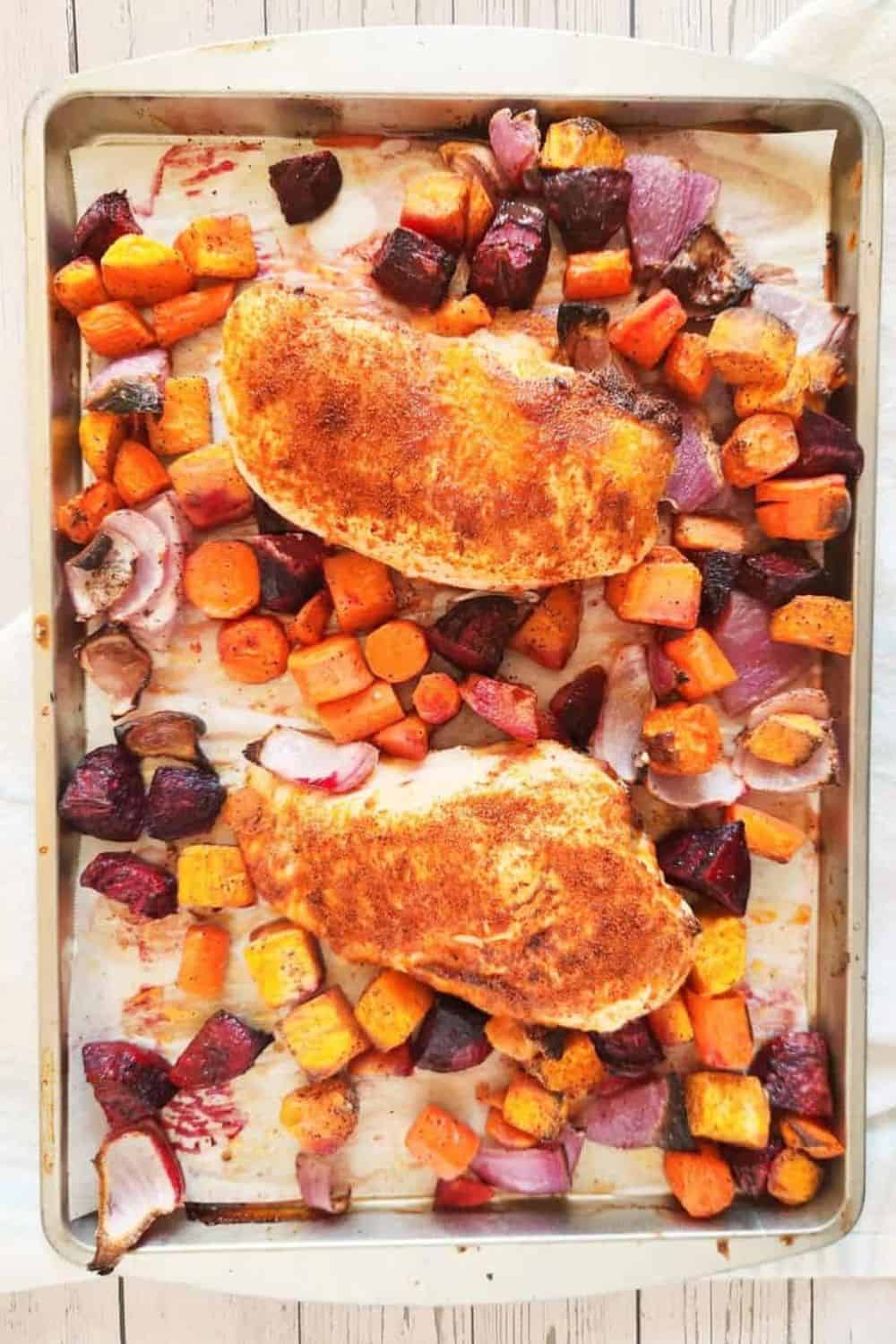 Roasted chicken with carrots, beets, and sweet potatoes, seasoned and cooked to perfection on a baking sheet.