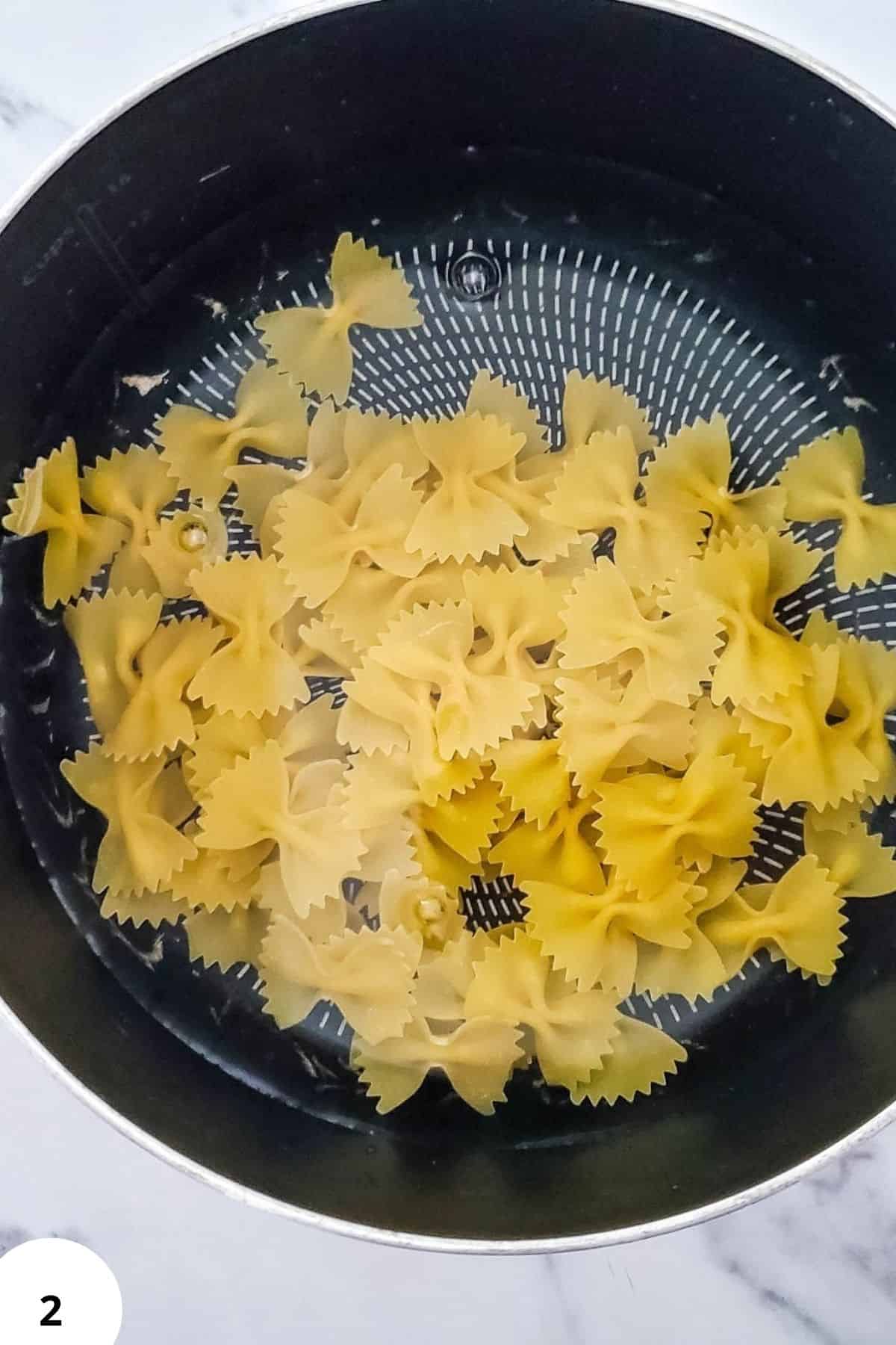 Farfalle or bow-tie pasta in a black colander, ready for cooking or serving.