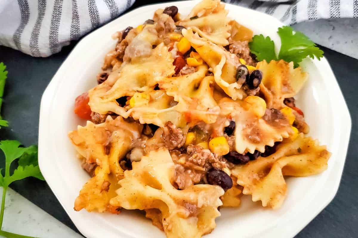 Delicious baked ziti with cheese, ground beef, black beans, and vegetables on a white plate.