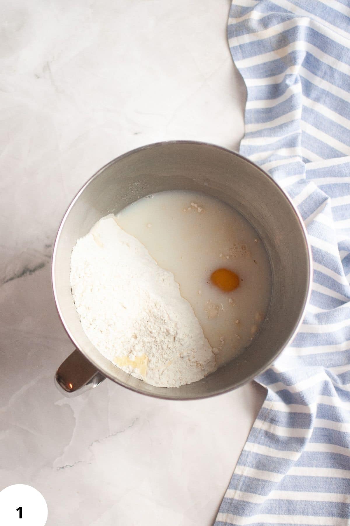 Homemade bread dough preparation using flour, eggs, and liquids in a stand mixer.