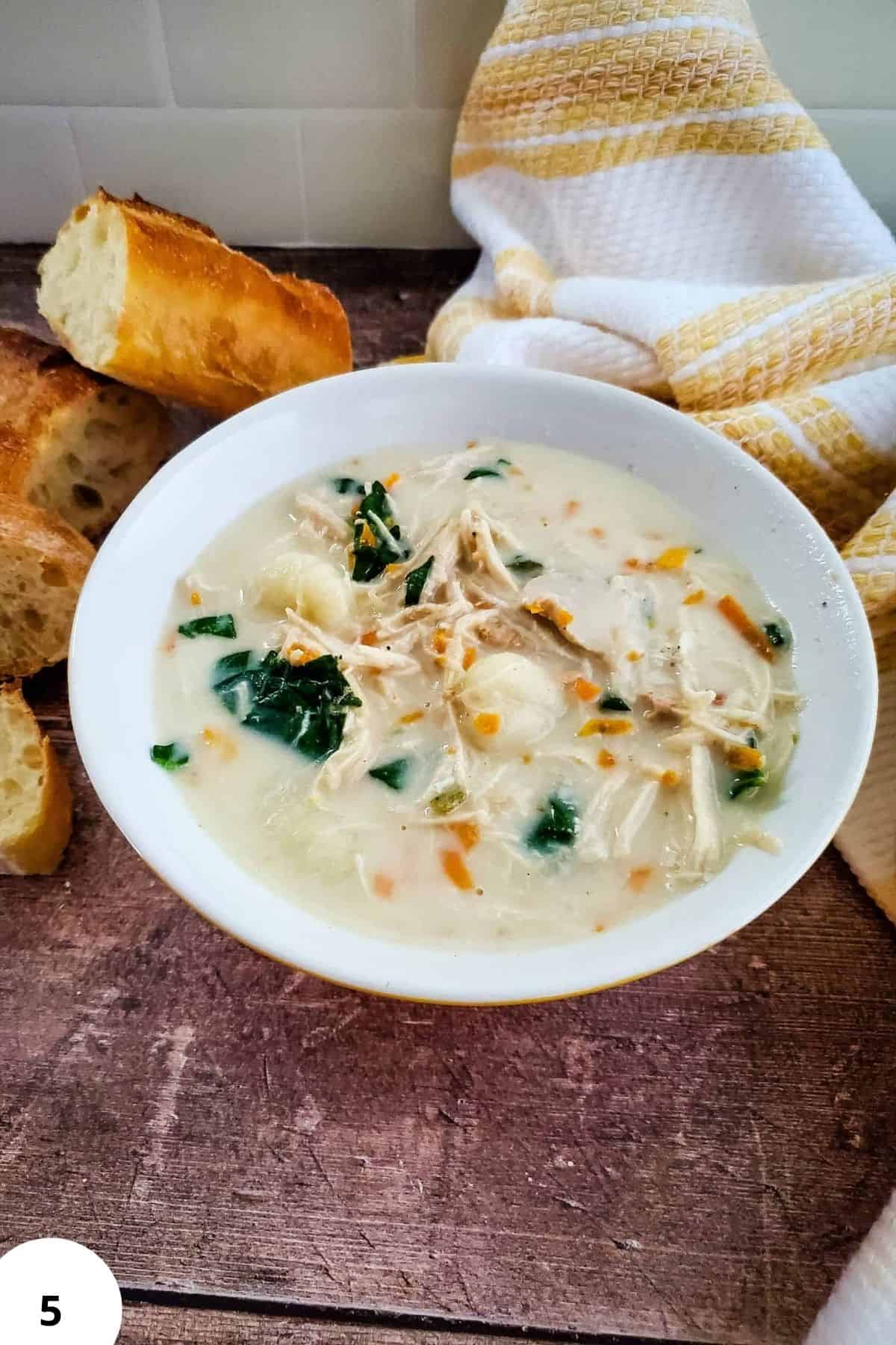 Comforting chicken and vegetable soup served in a white bowl, paired with artisan bread on a rustic wooden surface.