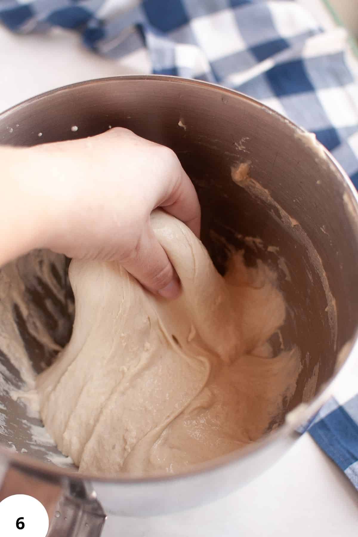 Close-up of hands kneading dough in a mixing bowl for homemade bread baking.