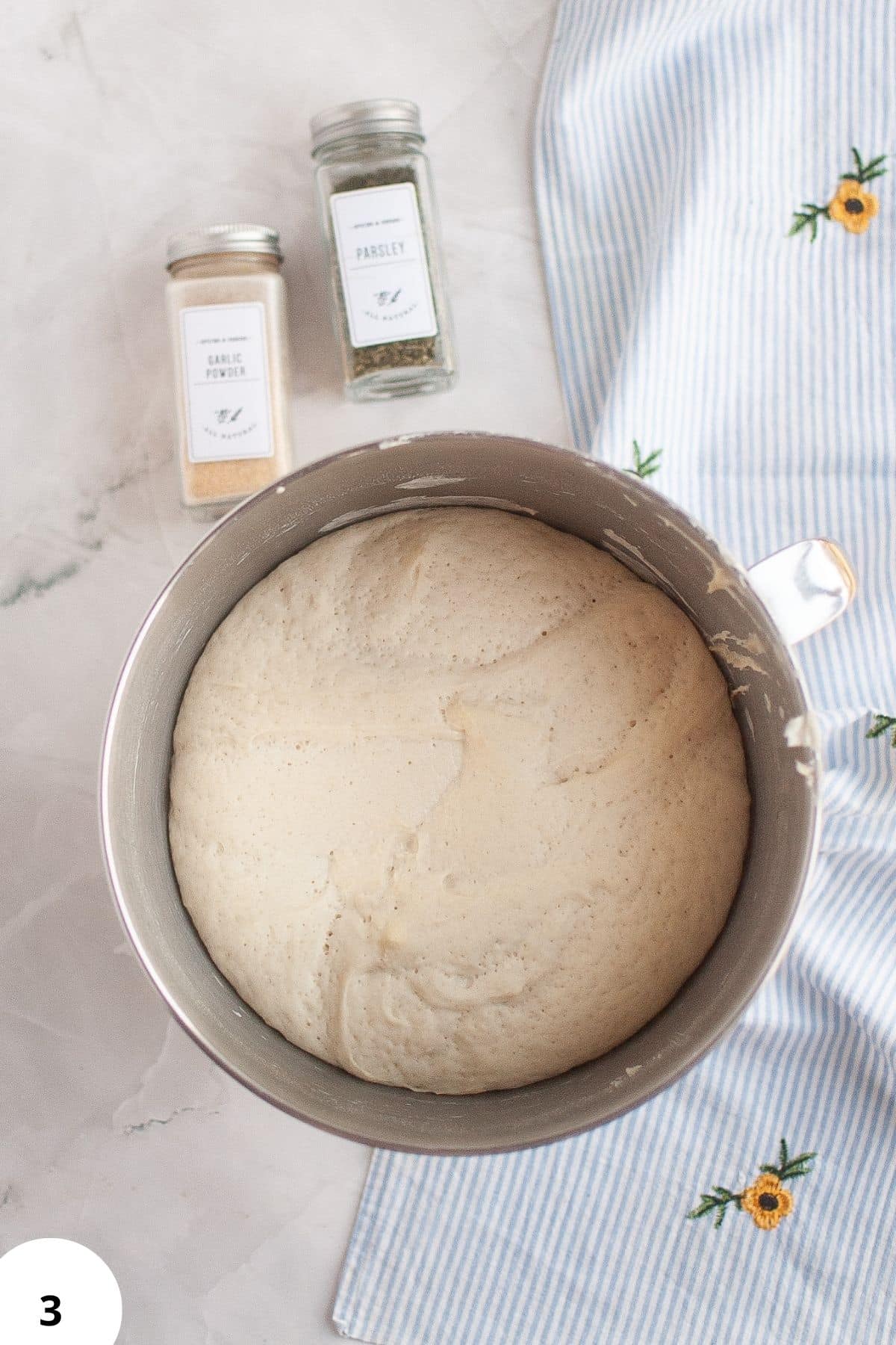 Delicious yeast dough rising in a mixing bowl with ingredients in jars nearby. Perfect for bread, pizza, and pastry recipes.