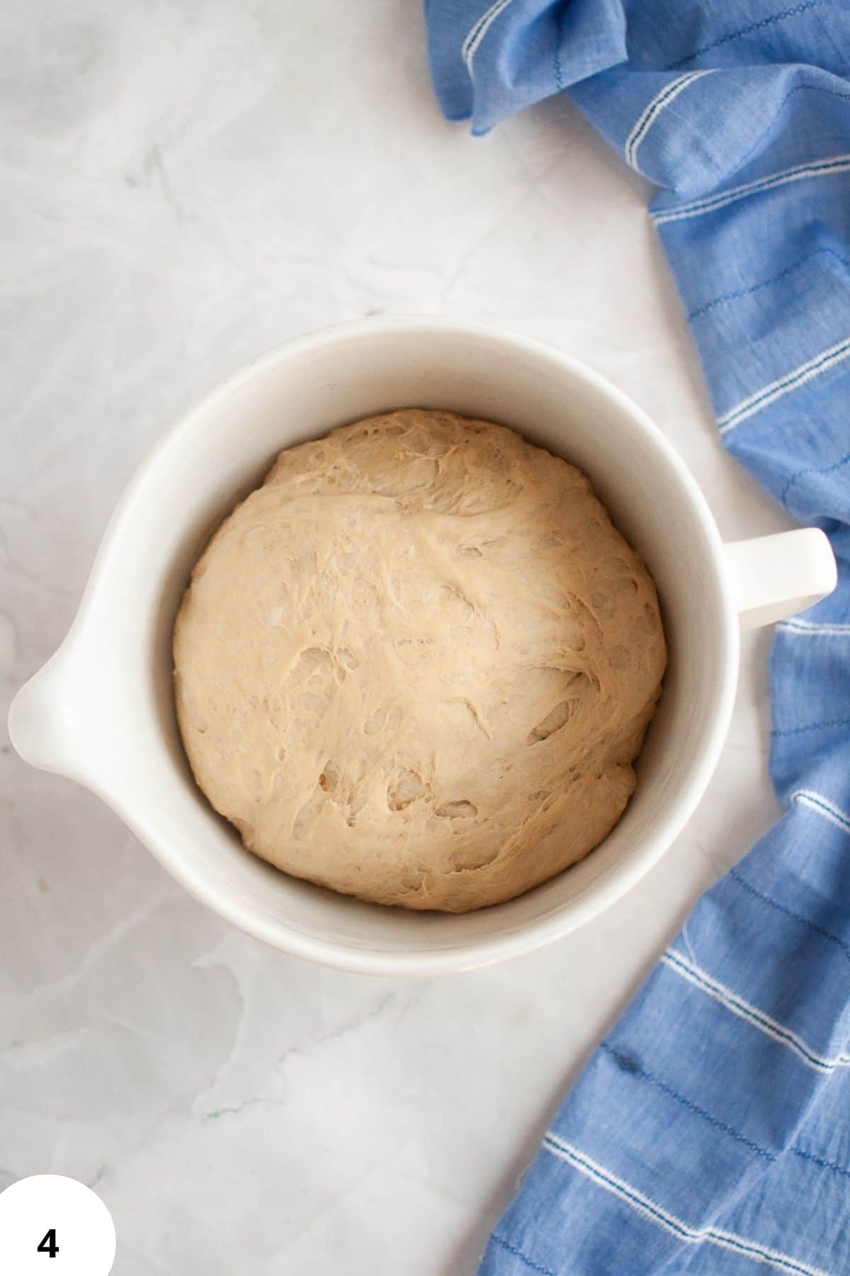 Soft, risen bread dough in a white mixing bowl for stretching and folding.