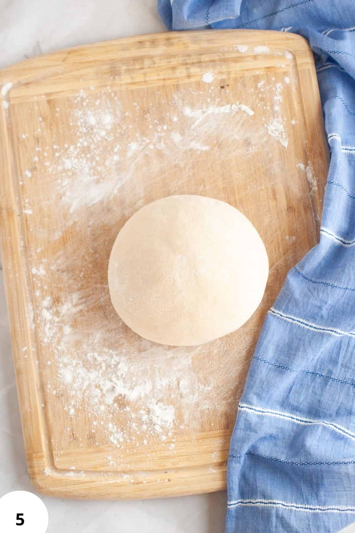 Freshly kneaded dough, ideal for bread making, with floured surface and blue cloth.