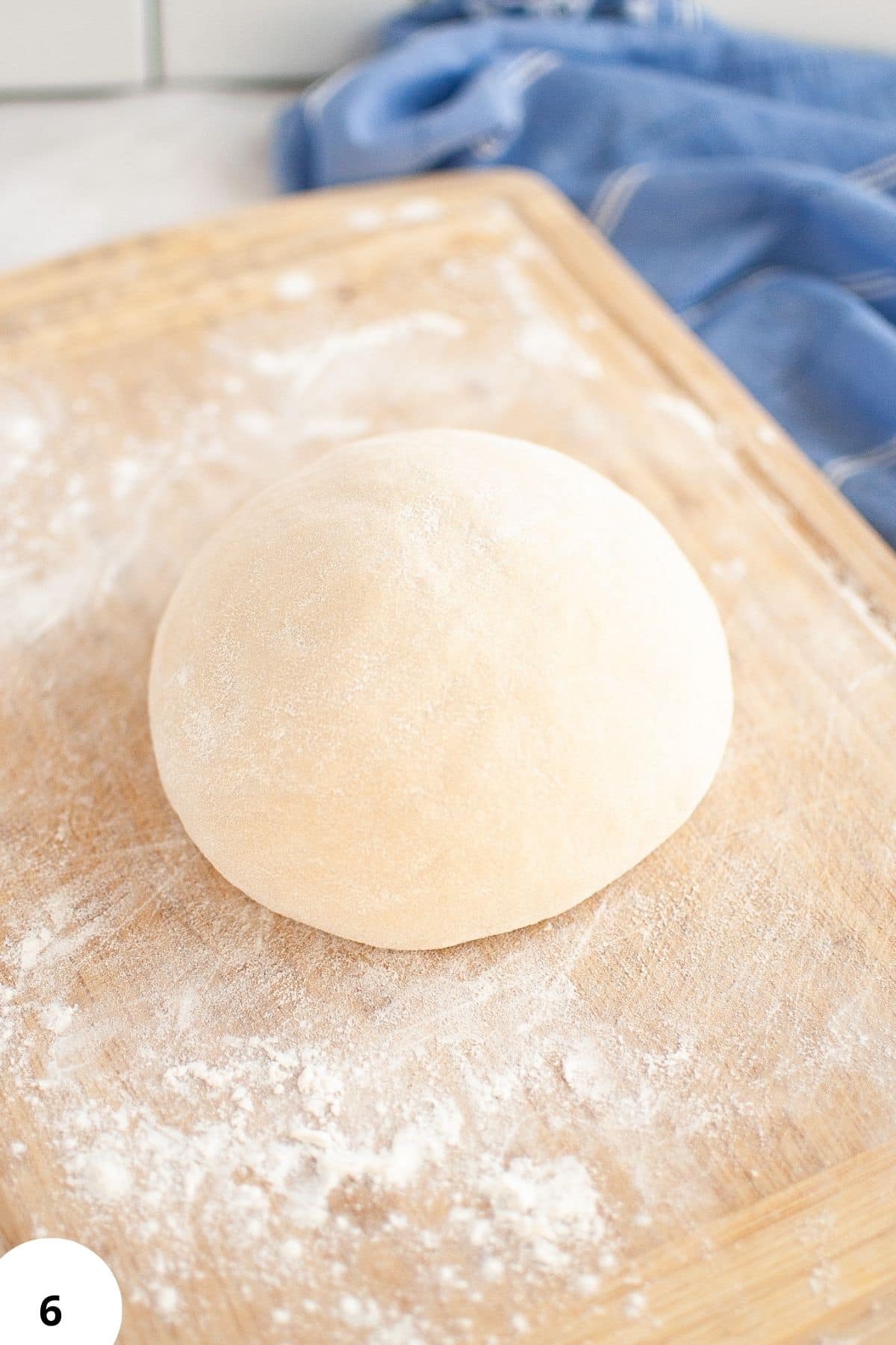 Alt text: Fresh bread dough ball resting on floured wooden surface for stretch and fold technique.