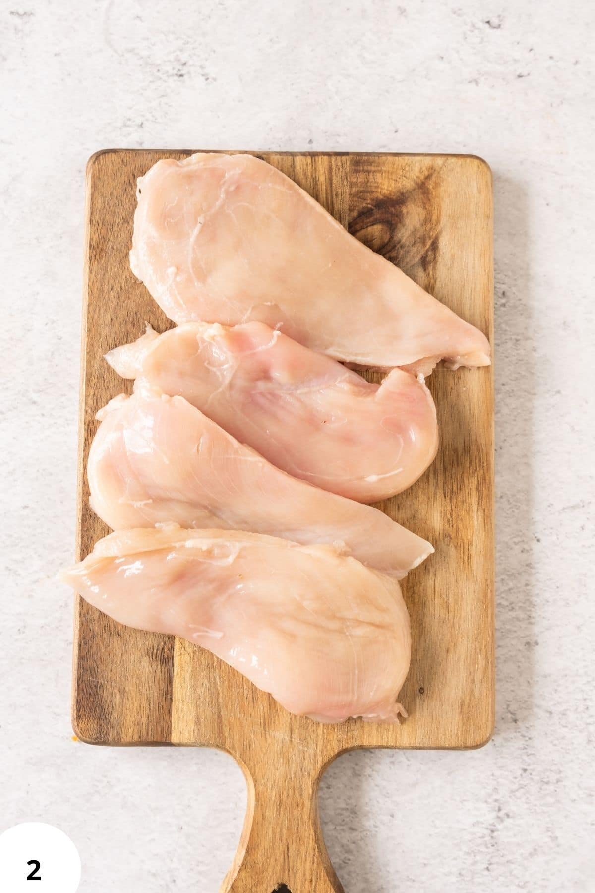Fresh chicken breasts on wooden cutting board for cooking and meal prep.