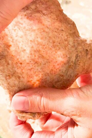 Close-up of a hand holding freshly milled grain bread, highlighting rustic texture and natural ingredients.