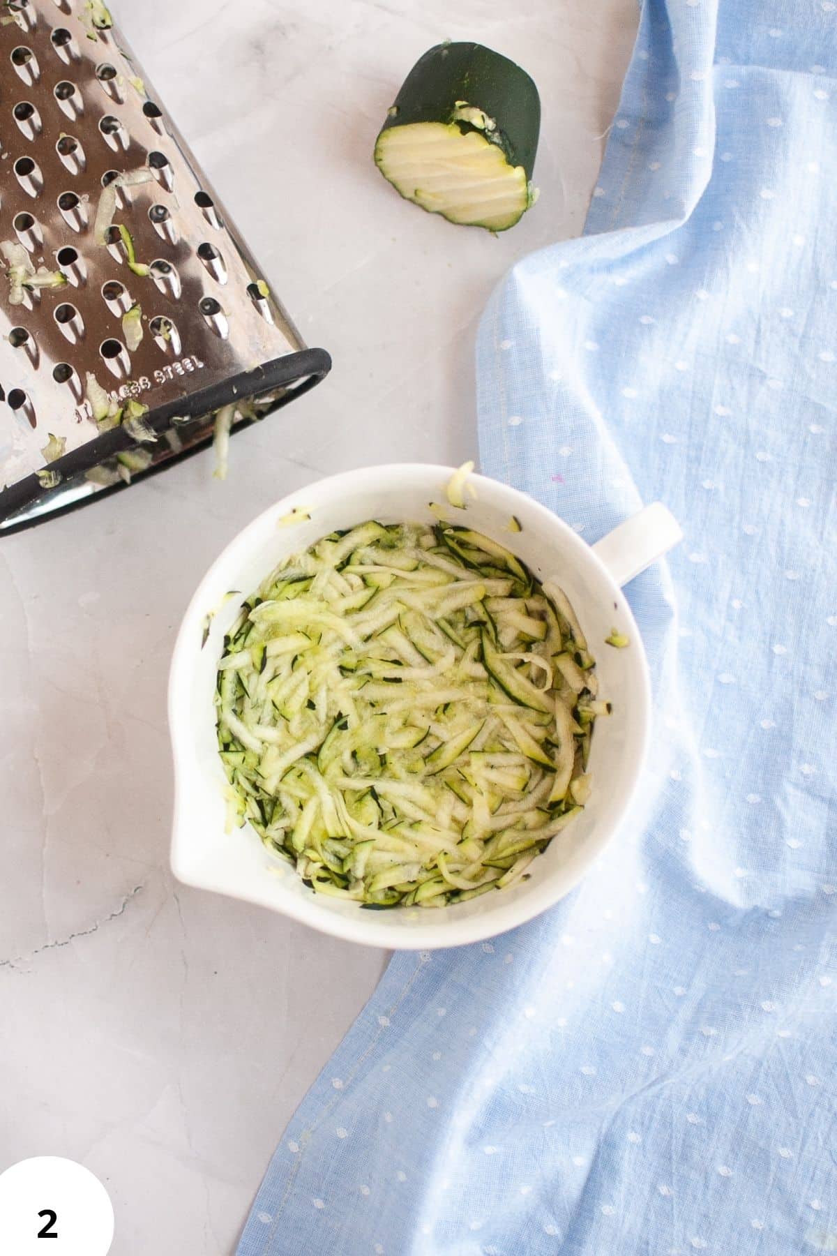 Zucchini shredded in a white bowl, ready for baking zucchini bread with walnuts.