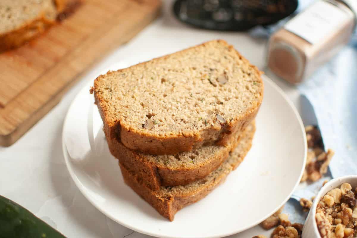 Sliced zucchini bread made with sourdough discard and walnuts on a white plate.