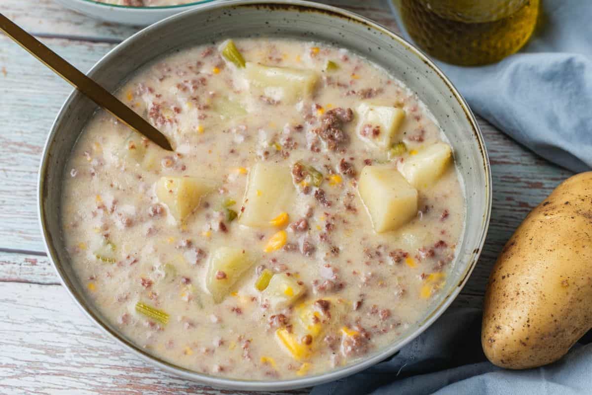Hearty hamburger and potato soup in a bowl with ingredients visible.