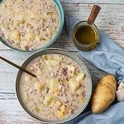 Hearty hamburger and potato soup in bowls with fresh ingredients and broth.
